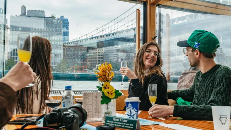 Guests with drinks at a window table overlooking a bridge on a New York architecture tour by yacht cruise
