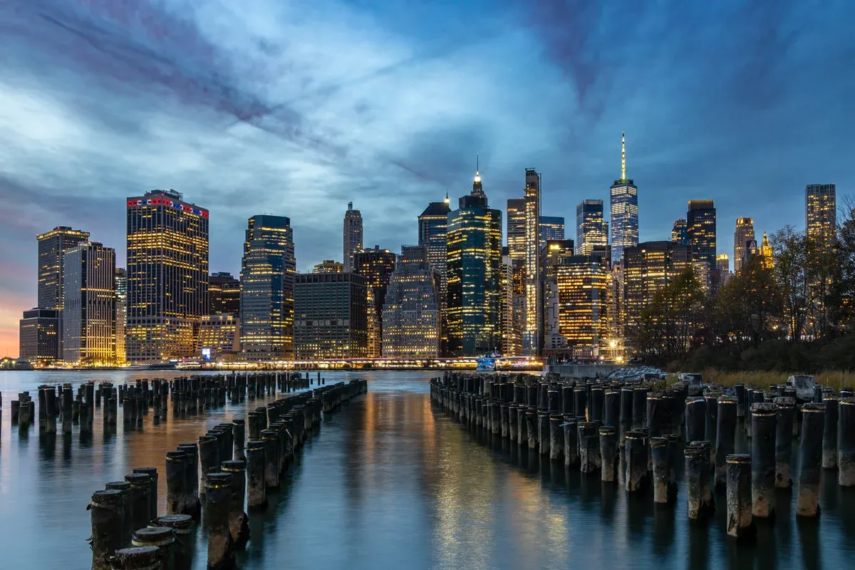 The lit towers of Lower Manhattan across the East River from Brooklyn Bridge Park at dusk, on a New York architecture tour